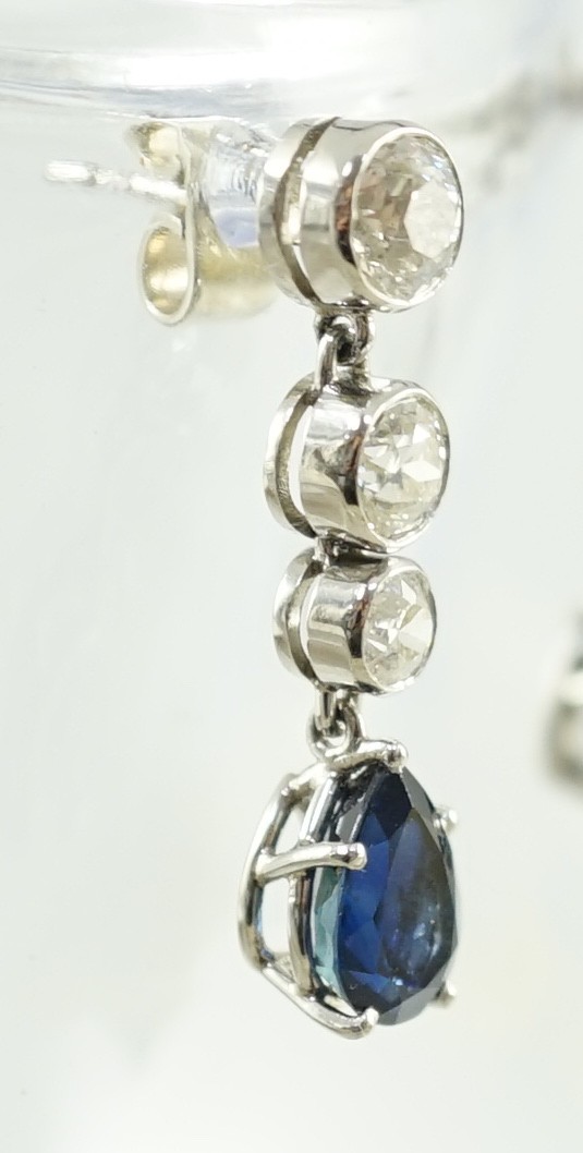 A pair of 1980's platinum, single stone pear cut sapphire and graduated three stone collet set diamond drop earrings